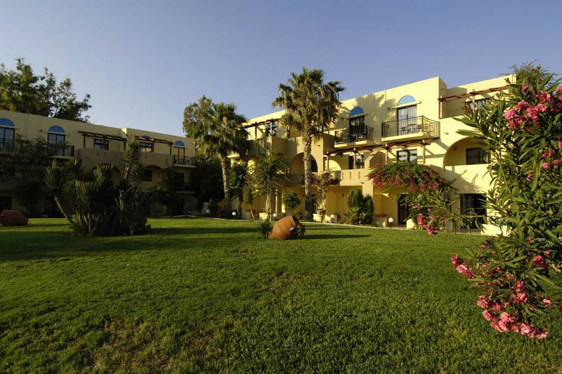 Außenansicht des gelben Porto Bello Beach Hotels mit grüner Rasenfläche und Blumen