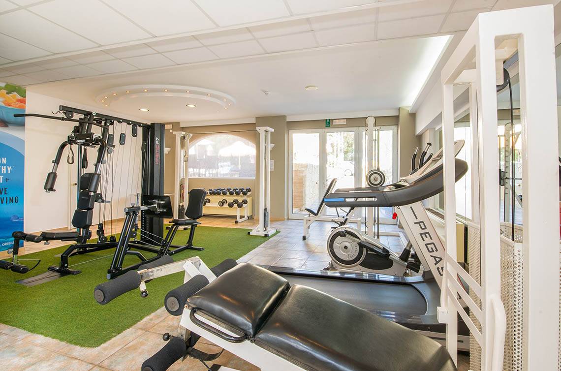 Fitnessraum im Kalyves Beach Hotel mit verschiedenen Geräten und grünem Teppich.