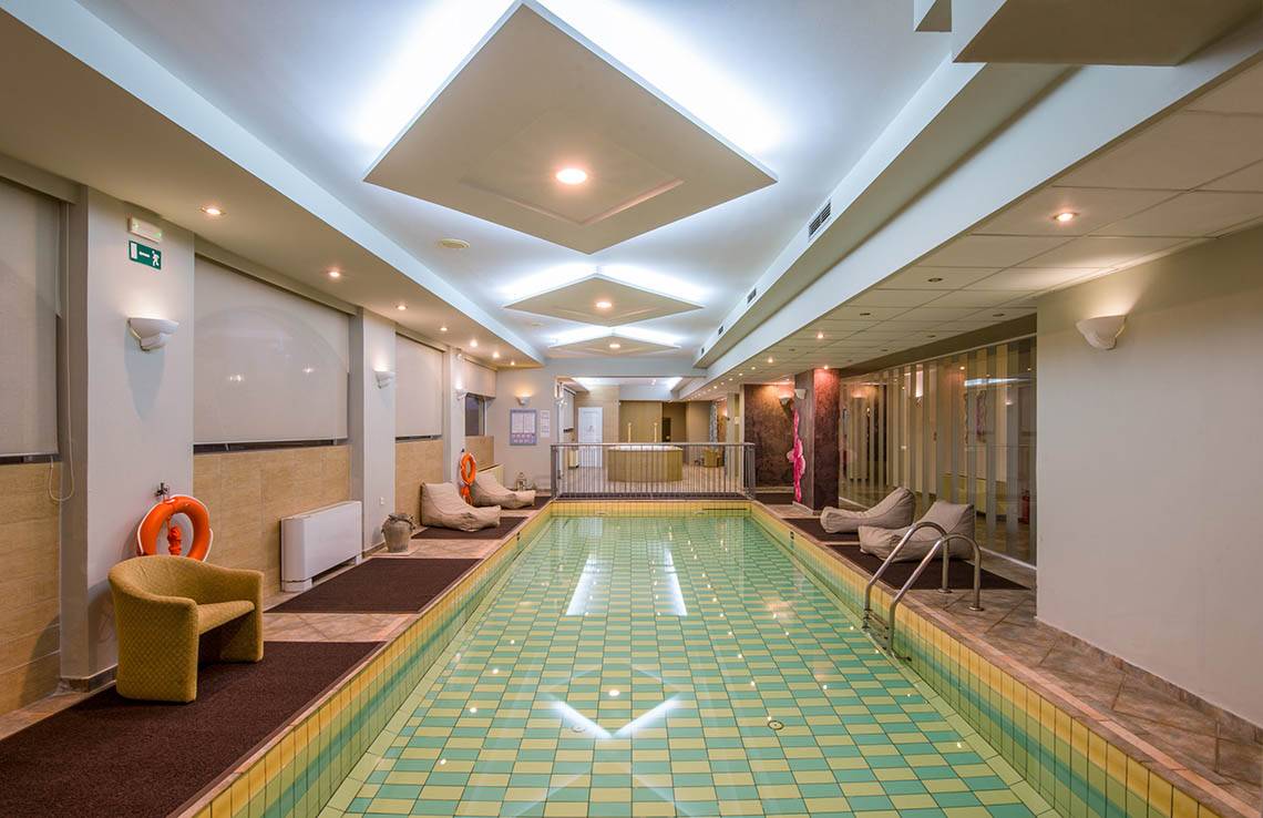 Innenpool des Kalyves Beach Hotels mit gefliesten Wänden und Sonnenliegen.