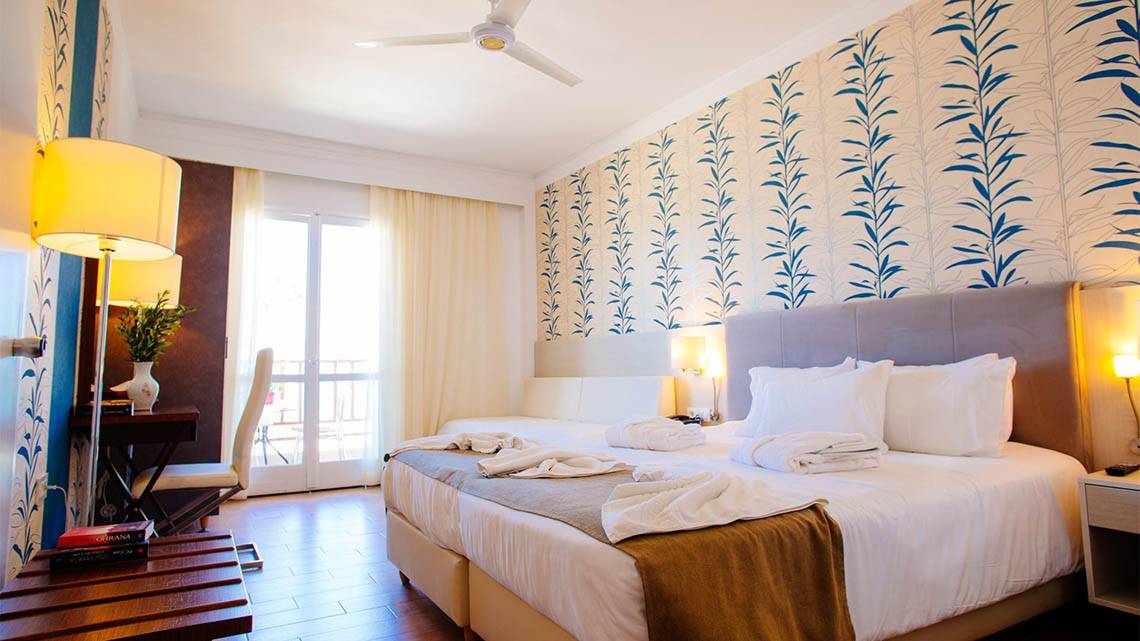 Innenansicht eines Doppelzimmers im Kalyves Beach Hotel mit blau-weißem Wandmuster und zwei Betten.