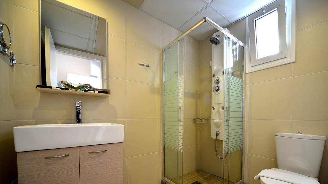 Badezimmer im Kalyves Beach Hotel mit Glasdusche, Waschbecken und Toilette.