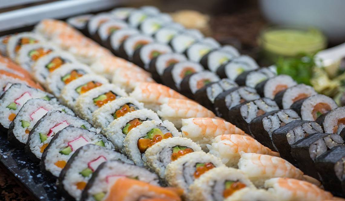 Eine Auswahl an verschiedenen Sushi-Rollen, die auf einem schwarzen Teller serviert werden.