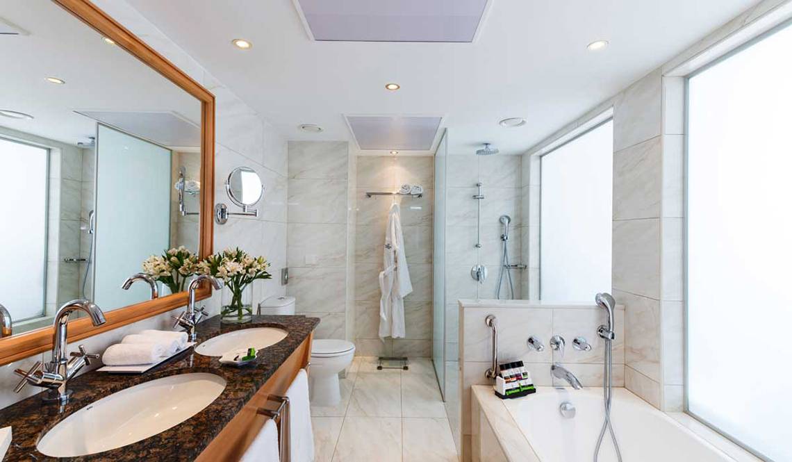 Badezimmer im Pioneer Beach Hotel mit Marmorfliesen, Doppelwaschbecken und Badewanne.