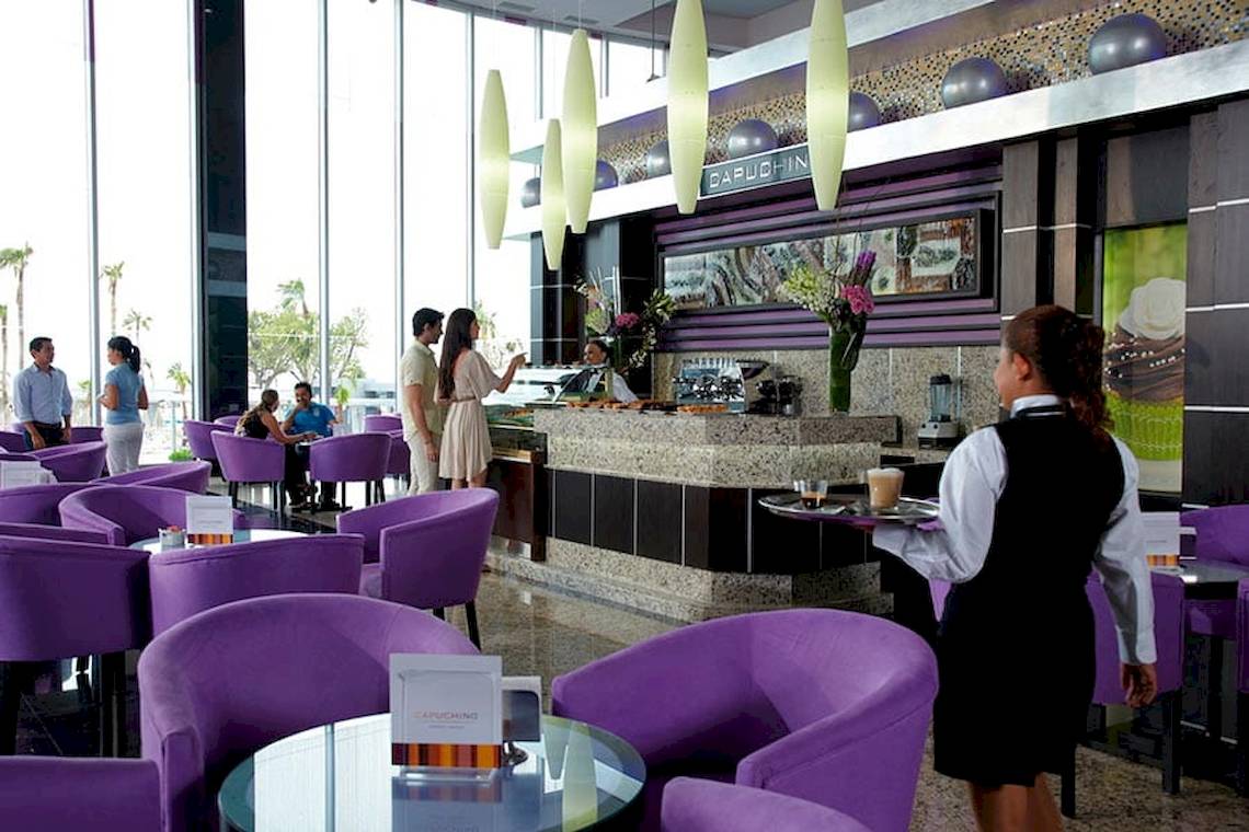 Hotellounge des Riu Palace Peninsula mit violetten Stühlen und einer Bar im Hintergrund.