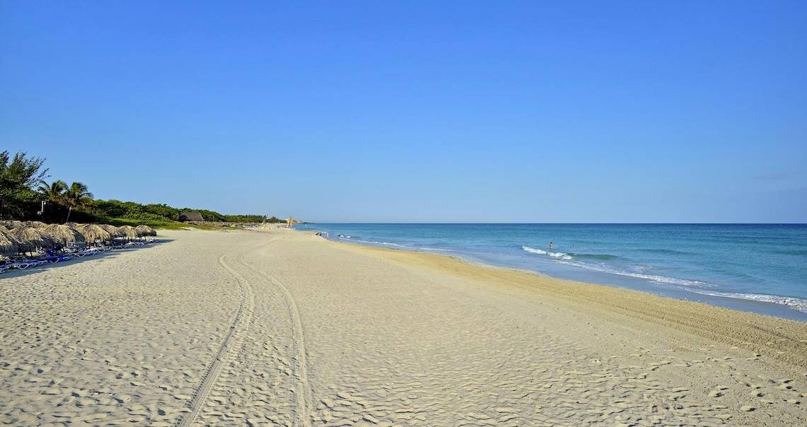 Strand des Melia Las Antillas Hotels mit weißen Sand, blauem Himmel und einigen Palmen.