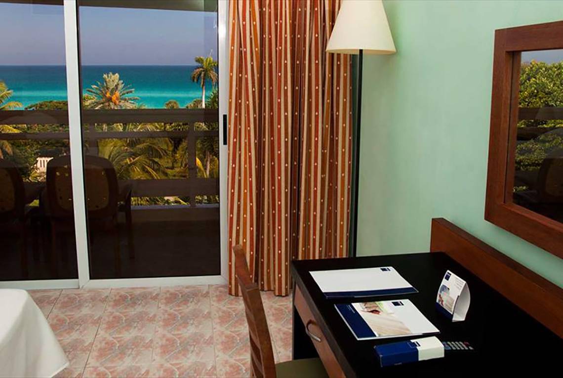 Zimmer im Occidental Arenas Blancas Hotel mit Meerblick, Glastür und Schreibtisch.