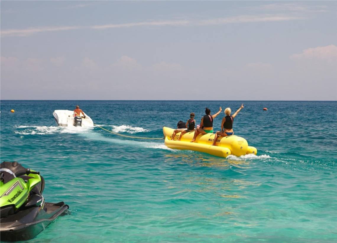 Mehrere Personen auf einem gelben Wassersport-Boot im Meer, gezogen von einem grünen Jetski.