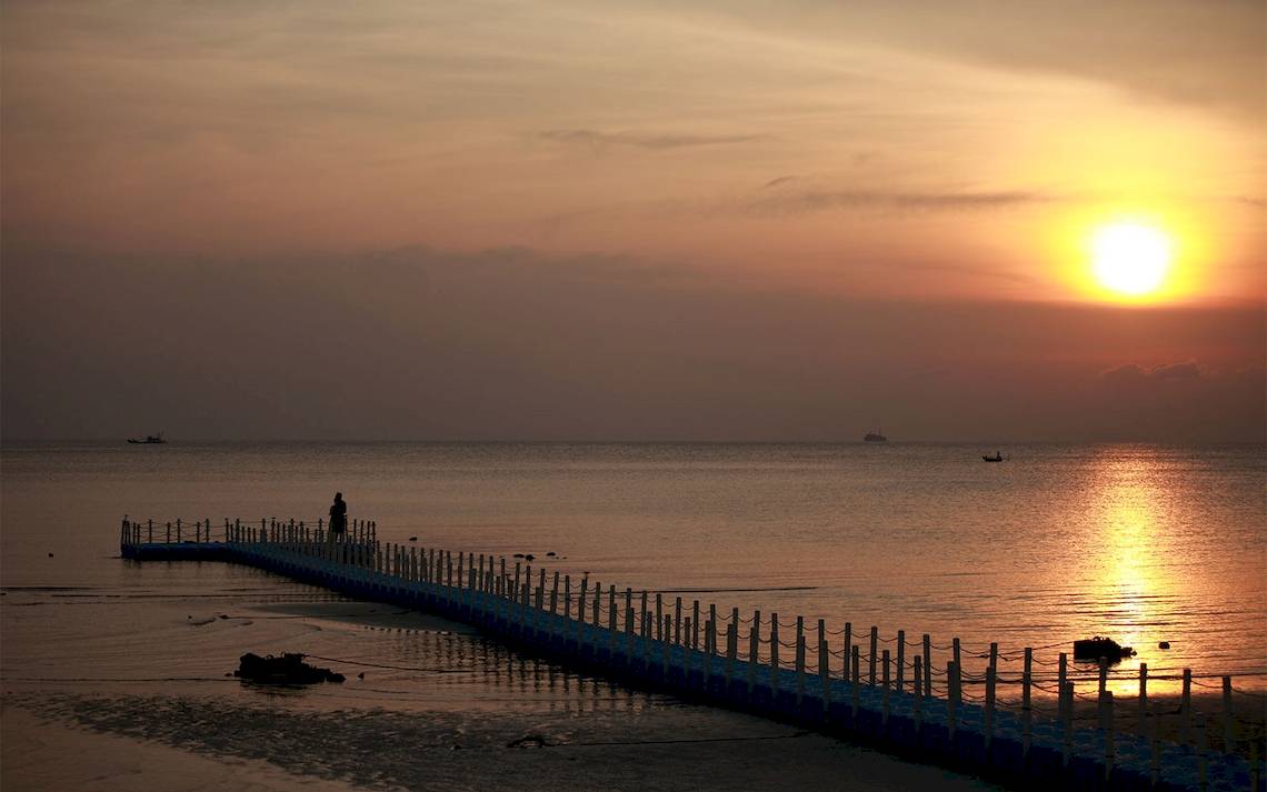 Sonnenuntergang am Strand mit Steg und Person
