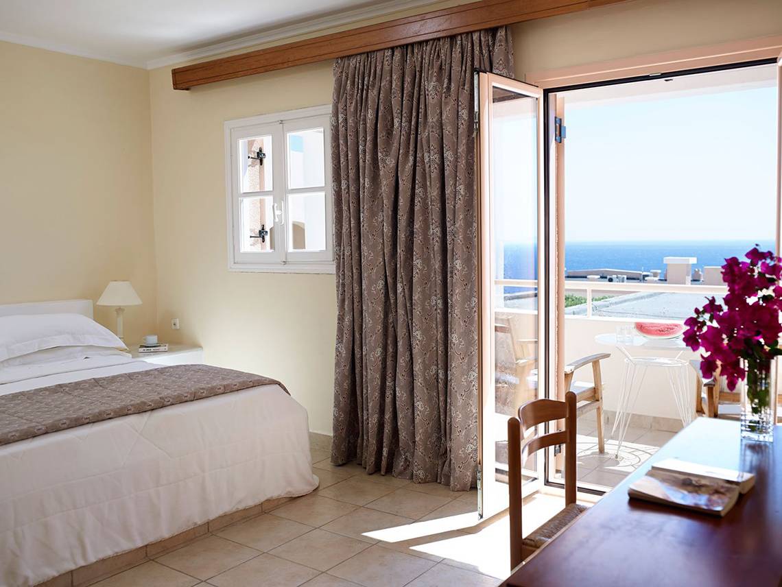 Zimmer im Mitsis Family Village Beach Hotel mit Balkon und Meerblick, Bett, Schreibtisch und Fenster.