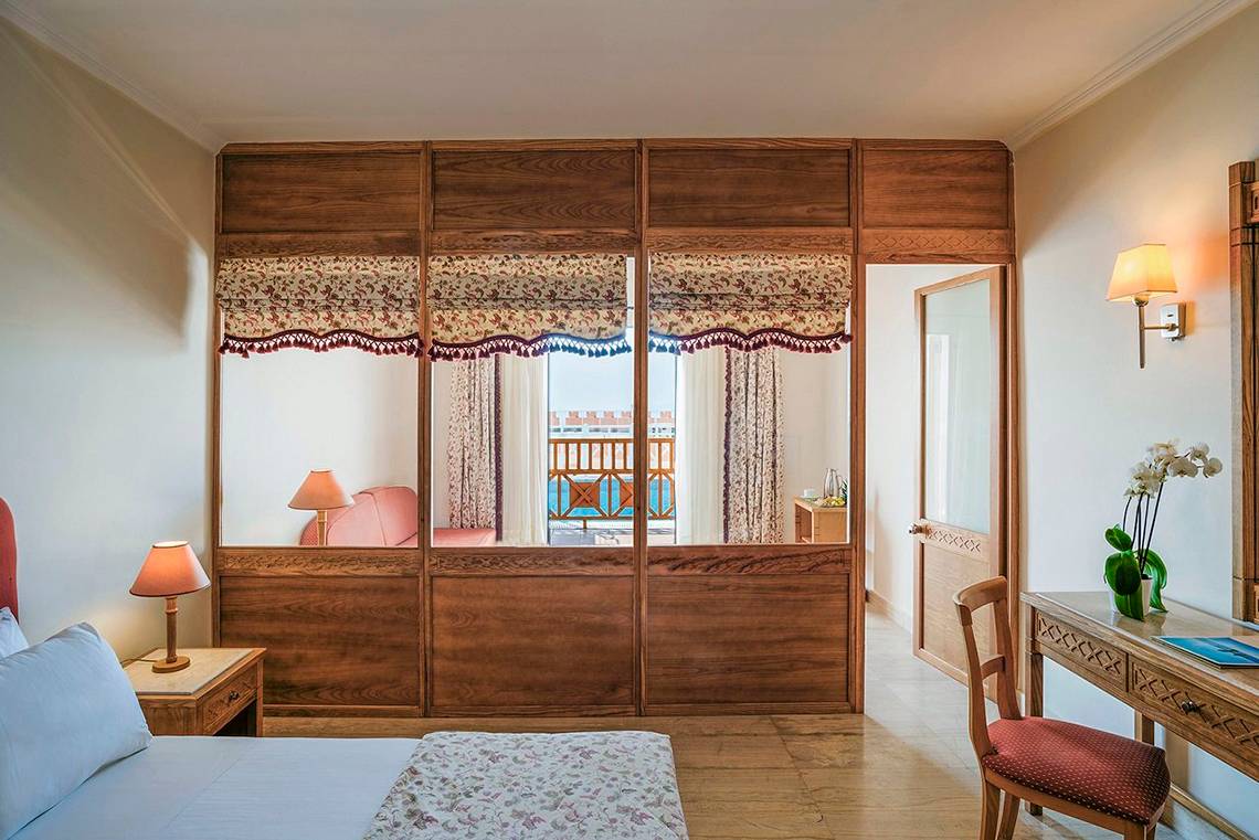 Innenansicht eines Zimmers im Mitsis Family Village Beach Hotel mit Blick auf eine Terrasse und das Meer.