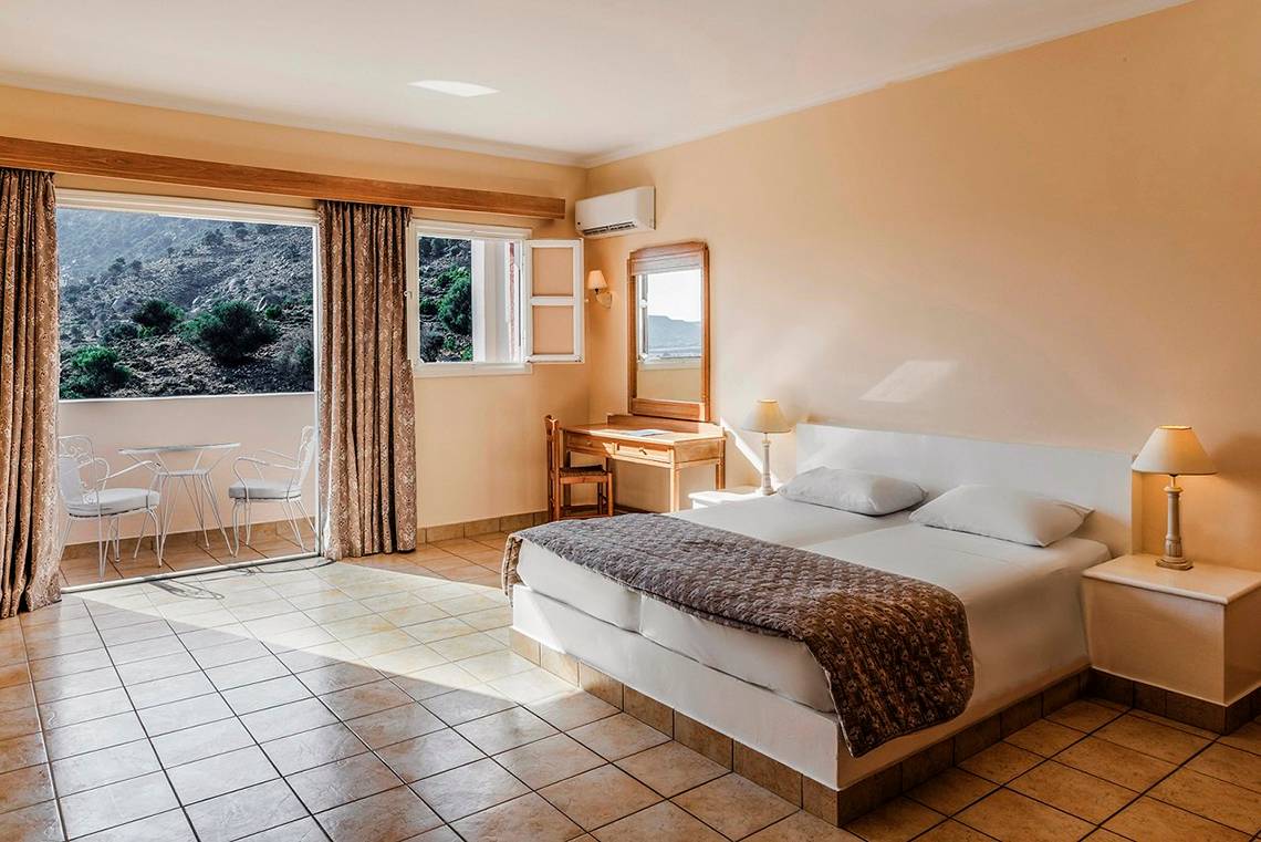 Innenansicht eines Zimmers im Mitsis Family Village Beach Hotel mit Bett, Schreibtisch und Balkon