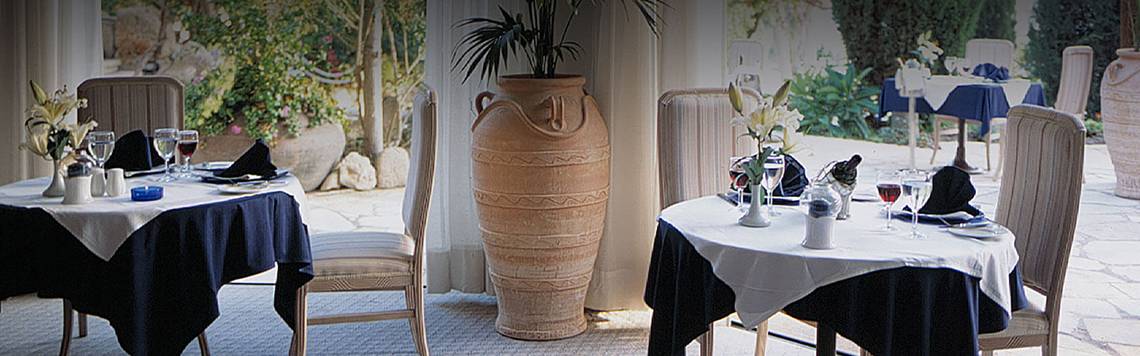 Innenansicht des Restaurants im Coral Beach Hotel mit Tisch, Stühlen und großen Vasen.