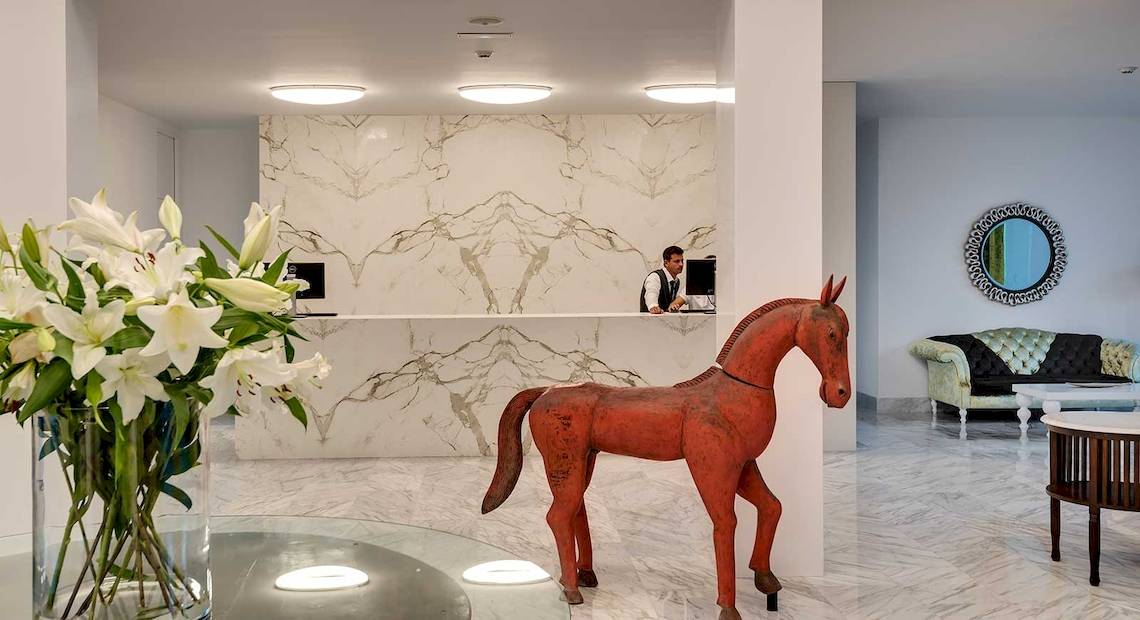 Lobby des Barceló Teguise Beach Adults Only Hotels mit Rezeption, rotem Pferdestatue und weißen Lilien im Glasvase.