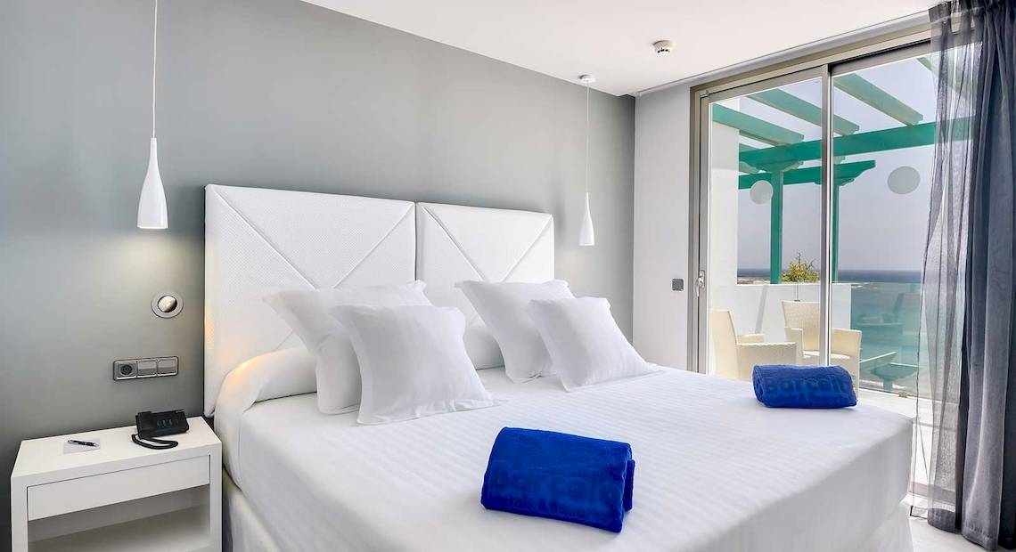 Zimmer im Barceló Teguise Beach Adults Only Hotel mit einem Bett, weißen Kissen und blauen Handtüchern.