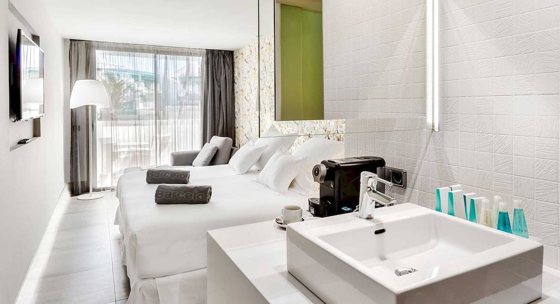Ein modernes Hotelzimmer im Barceló Teguise Beach Adults Only mit weißem Bett, Schreibtisch, Lampen und Badezimmer