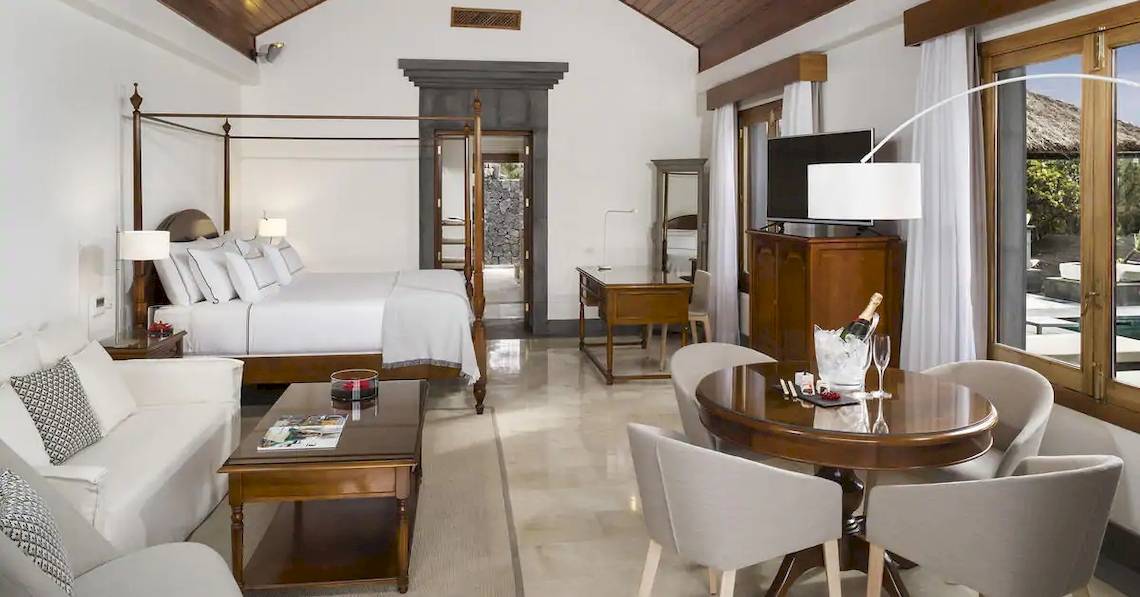 Innenansicht der Suite im Melia Salinas Hotel mit großem Bett, Wohnzimmerbereich und Esstisch.