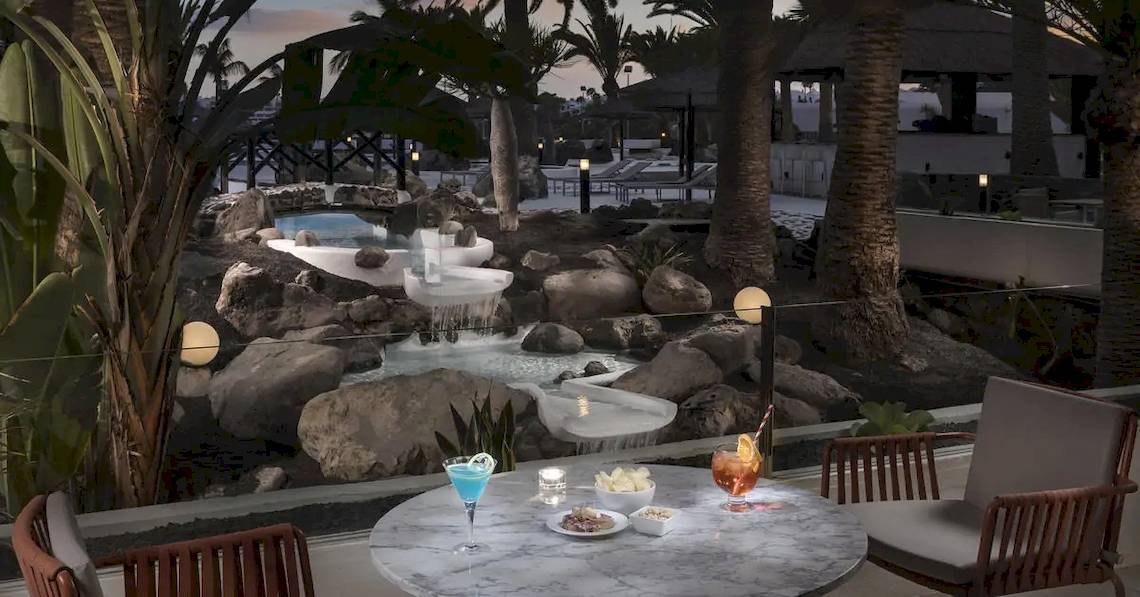 Terrasse im Melia Salinas Hotel mit Aussicht auf einen Wasserfall und Gartenlandschaft.