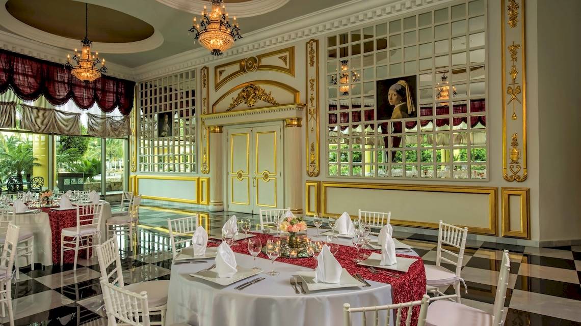 Speisesaal im Iberostar Grand Paraiso mit runden Tischen, eleganten Stühlen und Goldverzierungen.