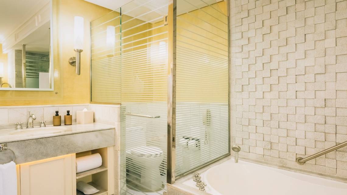 Badezimmer im Iberostar Grand Paraiso Hotel mit gelben Wänden, Marmorboden, Badewanne, Dusche und Toilette.