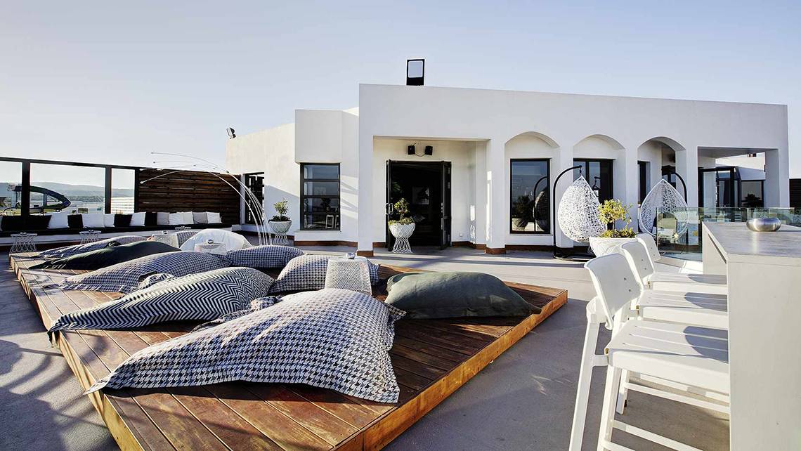 Die Dachterrasse des Club Plimmiri Hotels mit weißen Möbeln und Kissen, umgeben von Pflanzen.