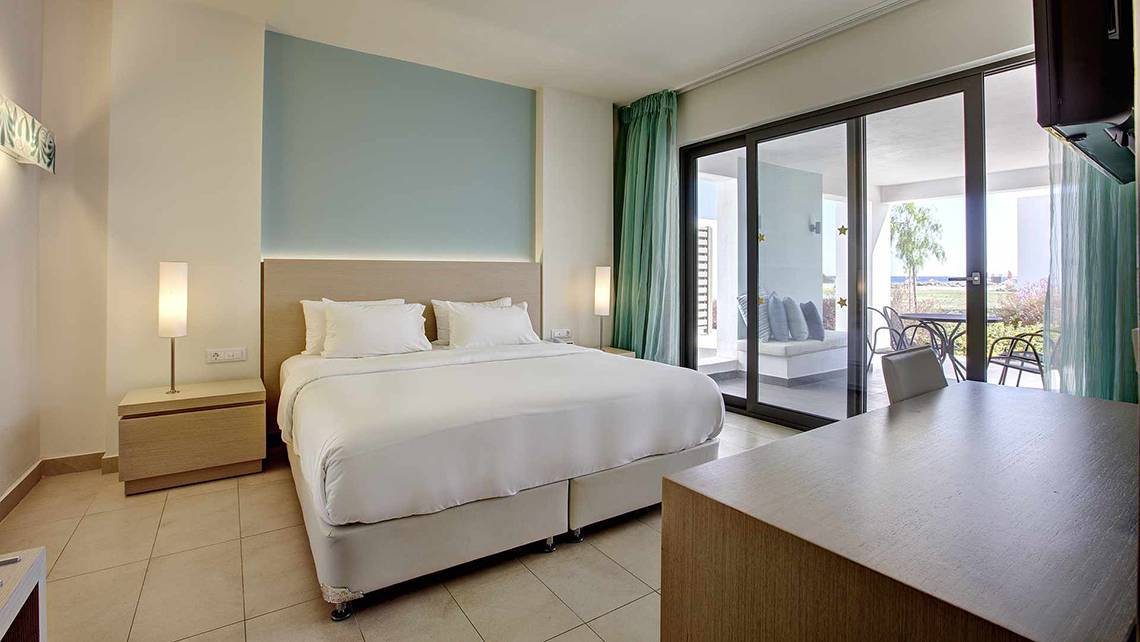 Innenansicht eines Hotelzimmers im Club Plimmiri Hotel mit Bett, Nachttischen und einer Terrasse davor.