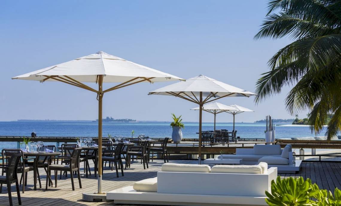 Terrasse des Outrigger Maldives Maafushivaru Resorts mit Blick auf das Meer und weißen Möbeln.