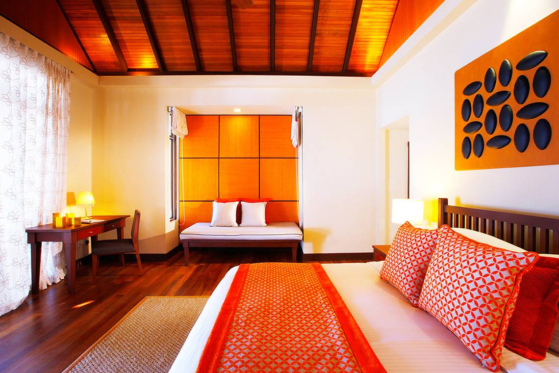 Innenansicht des Schlafzimmers im Kurumba Maldives Hotel mit Bett, Schreibtisch und Wanddekoration.