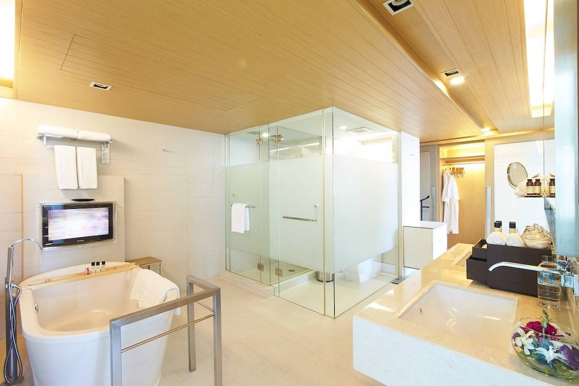 Badezimmer im Pathumwan Princess Hotel mit Badewanne, Glasdusche und Fernseher.