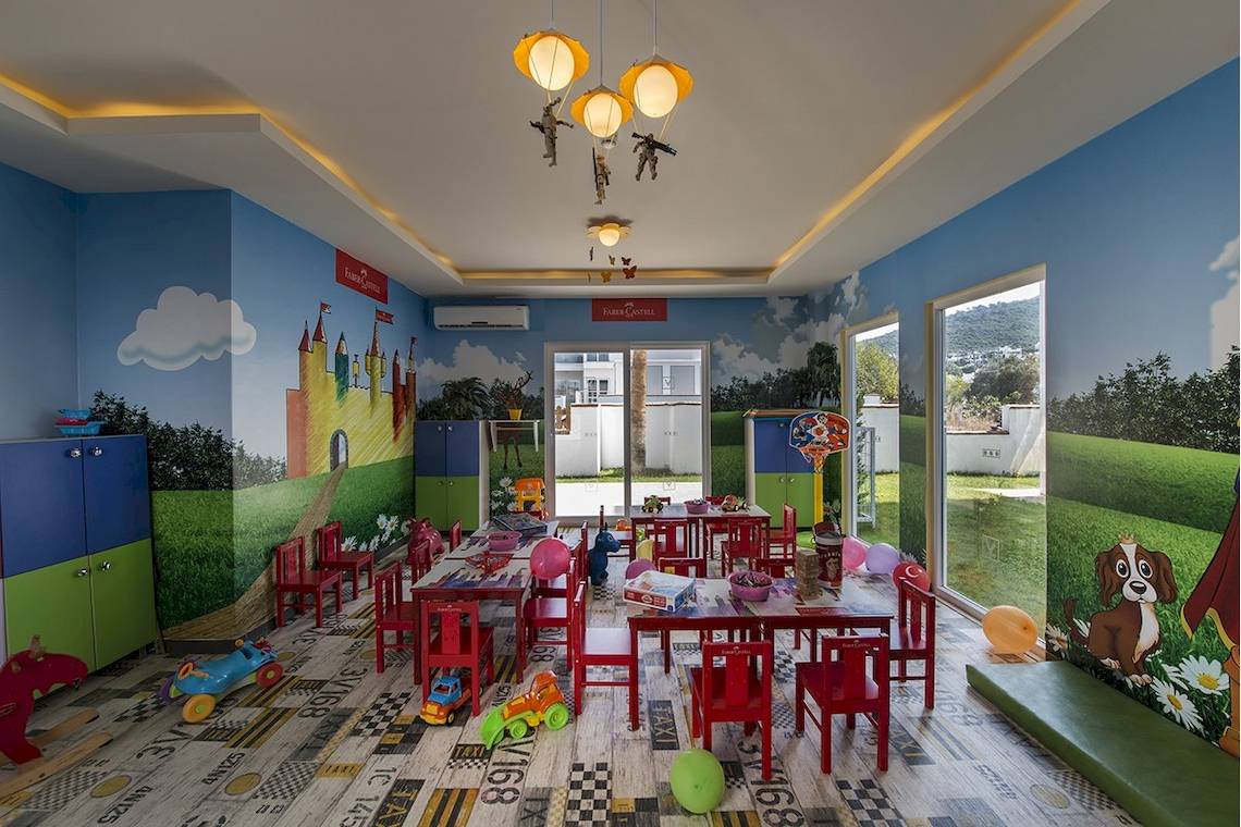 Voyage Torba Kinderzimmer mit bunten Wänden, Spielzeug und roten Stühlen.