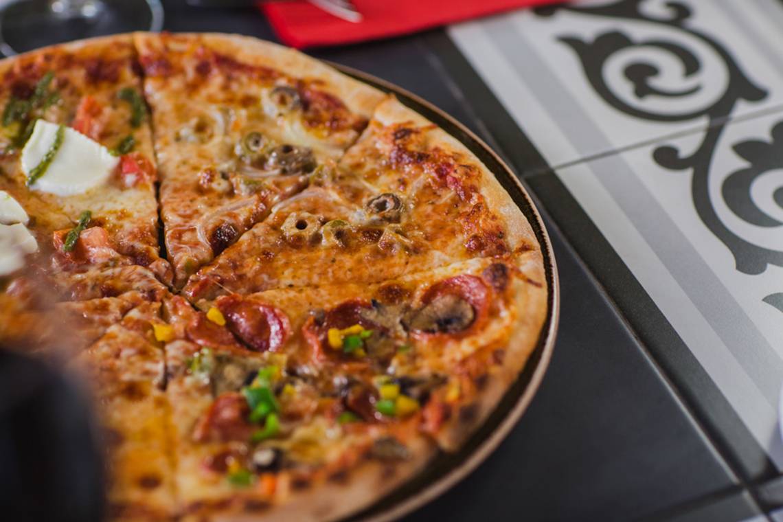 Eine Pizza mit diversen Belag, wie Peperoni, Zwiebeln und Pilzen, auf einem Tisch.