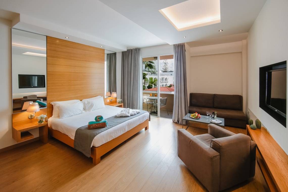 Schlafzimmer im Napa Plaza Hotel mit Doppelbett, Sofa, Fernseher und Balkonzugang.