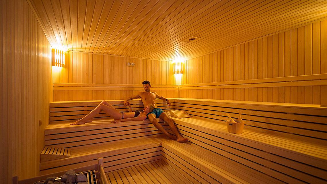 Paar in der Sauna im Terrace Elite Resort, entspannt auf Holzbänken sitzend.