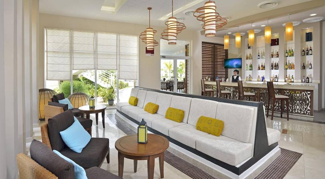 Loungebereich im Paradisus Princesa del Mar Resort & Spa mit einer gepolsterten Bank, Stühlen und einem Barbereich.
