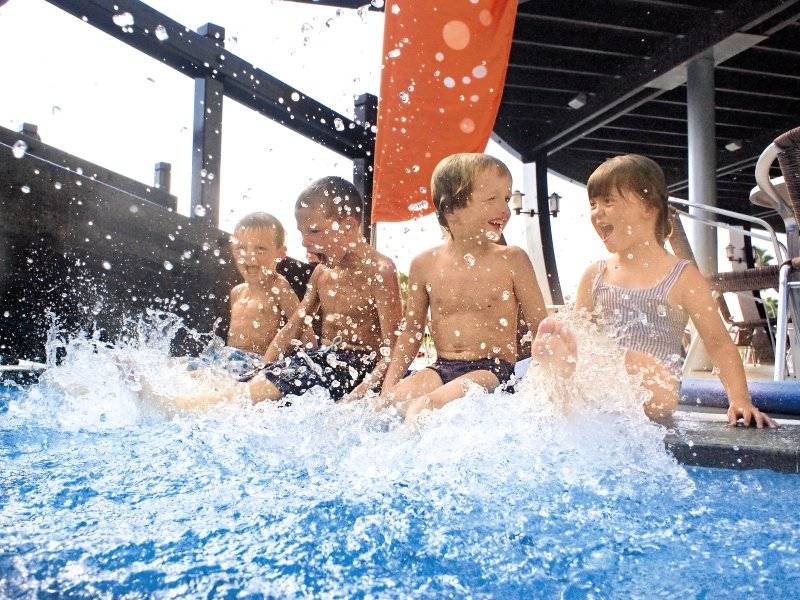 Vier Kinder sitzen im Pool und spielen vergnügt im Wasser.