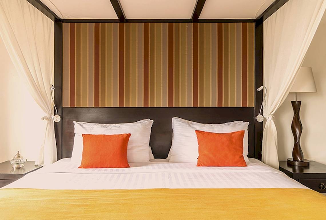 Bett im Jetwing Sea Hotel mit orangen Kissen und gestreiften Kopfteil.