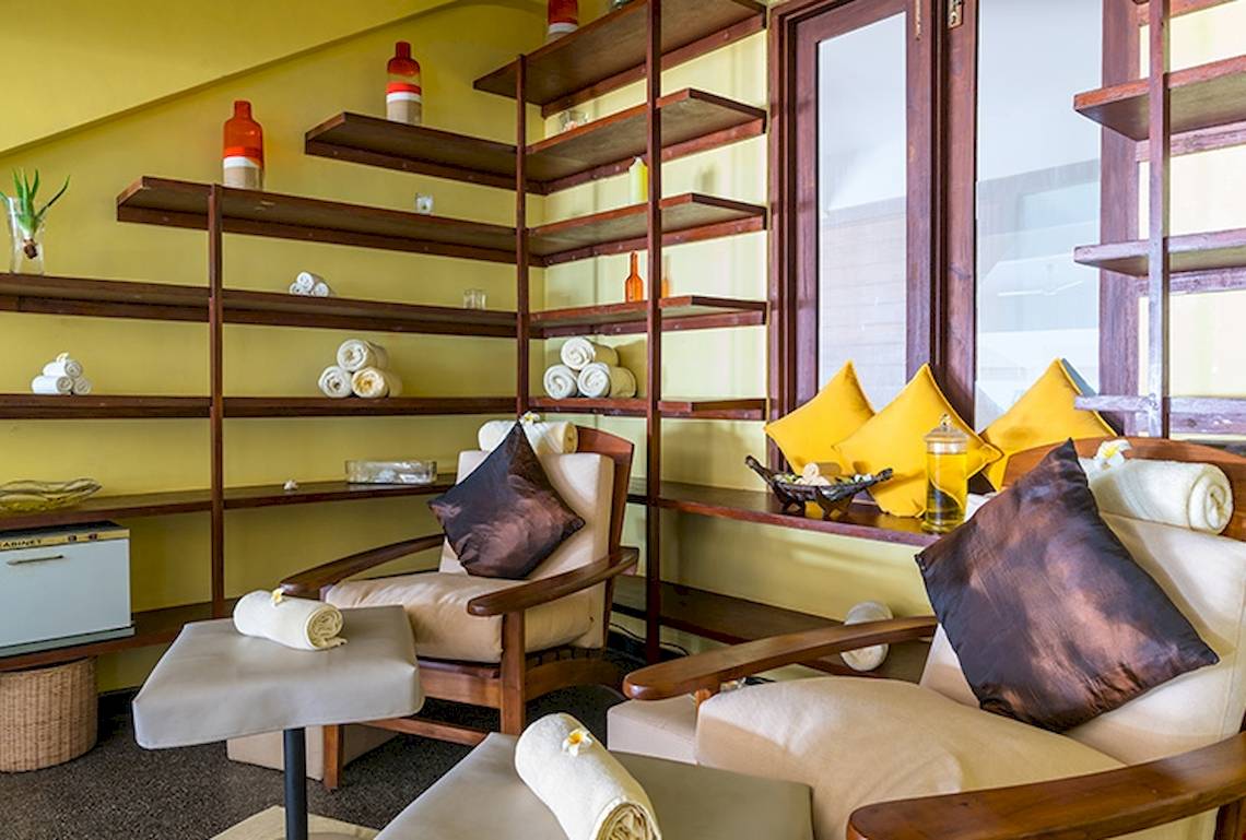 Innenansicht des Massageraums im Jetwing Sea Hotel mit Holzmöbeln, Kissen und Regalen mit Pflegeprodukten.
