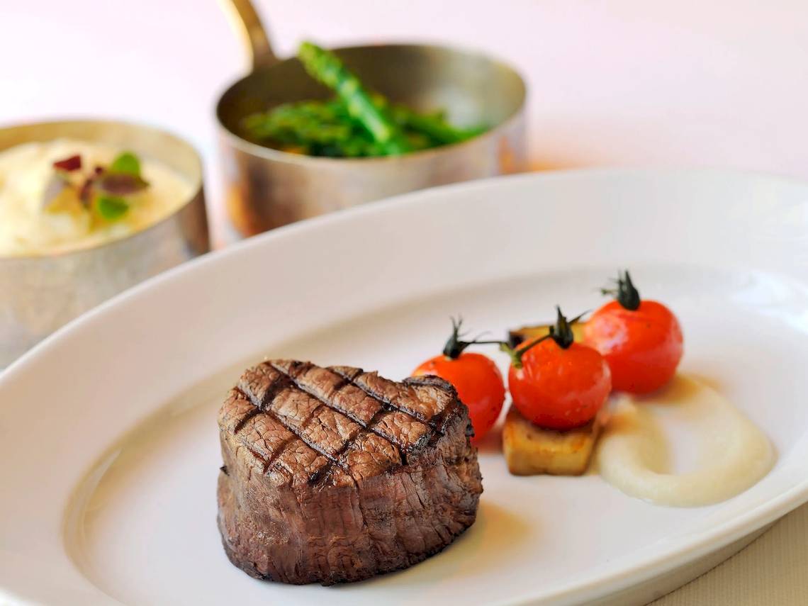 Ein Steak auf einem weißen Teller im Park Hyatt Abu Dhabi Hotel & Villas, neben Tomaten und Beilagen.