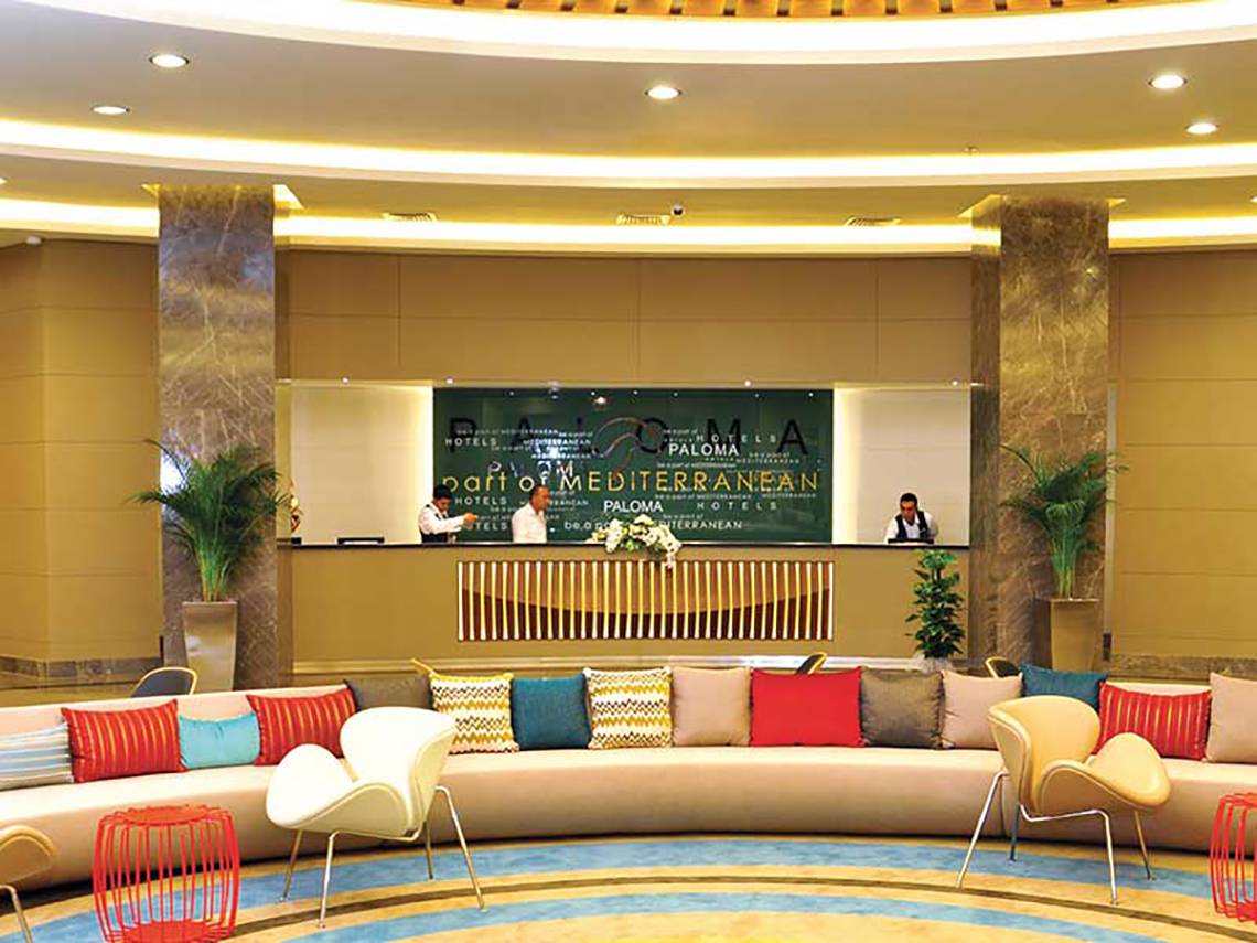 Empfangsbereich des Paloma Oceana Hotels mit bunten Kissen und Pflanzen.