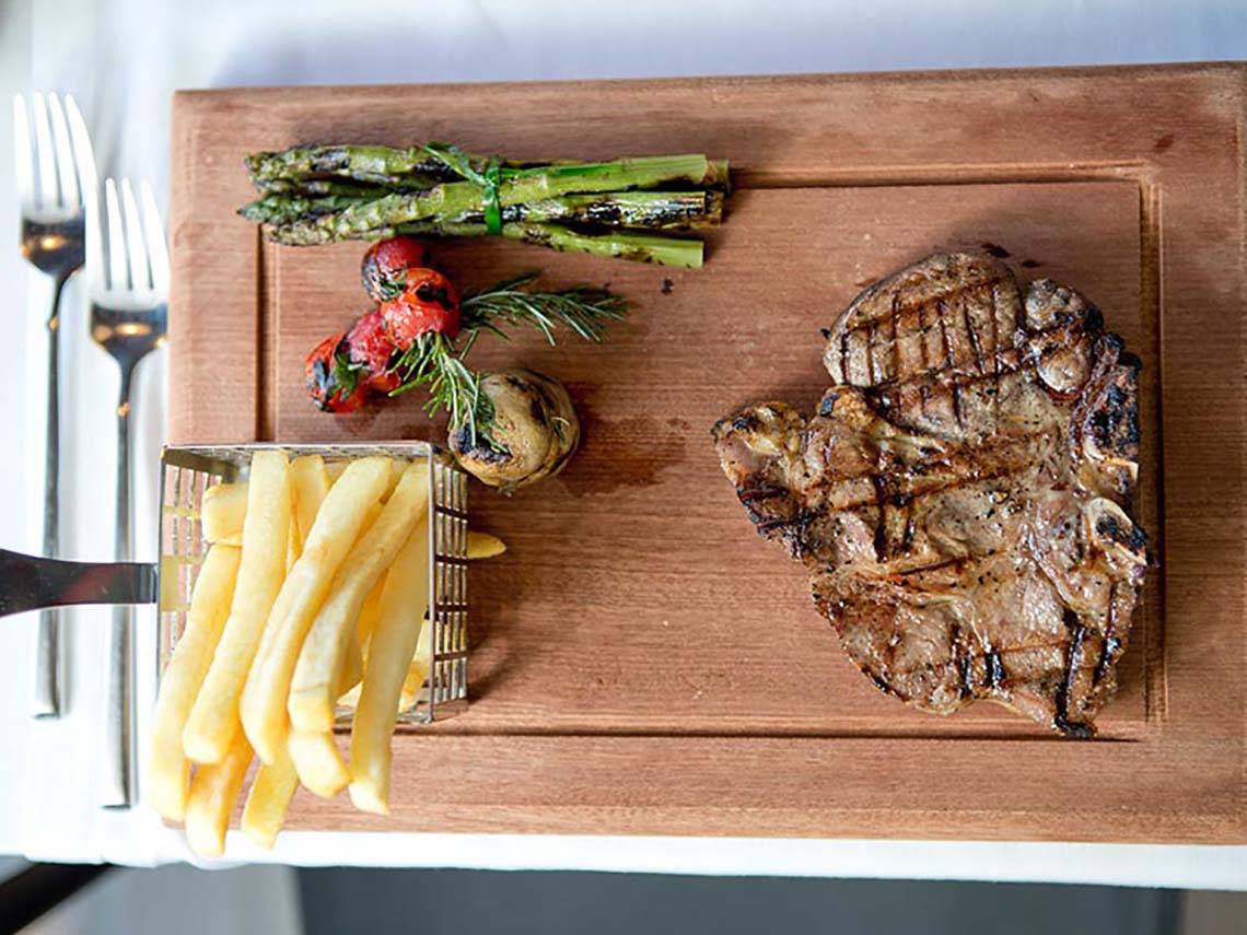 Ein Steak-Teller mit Pommes, Spargel, Tomaten und Rosmarin auf einem Holzbrett.