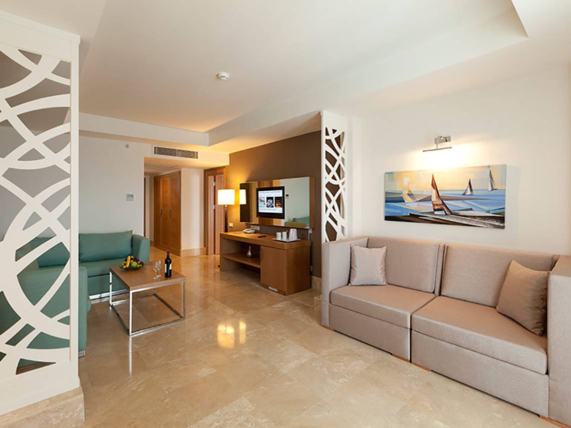 Wohnbereich im Paloma Oceana Hotel mit Sofa, Couch, Tisch, Fernseher und Gemälde.