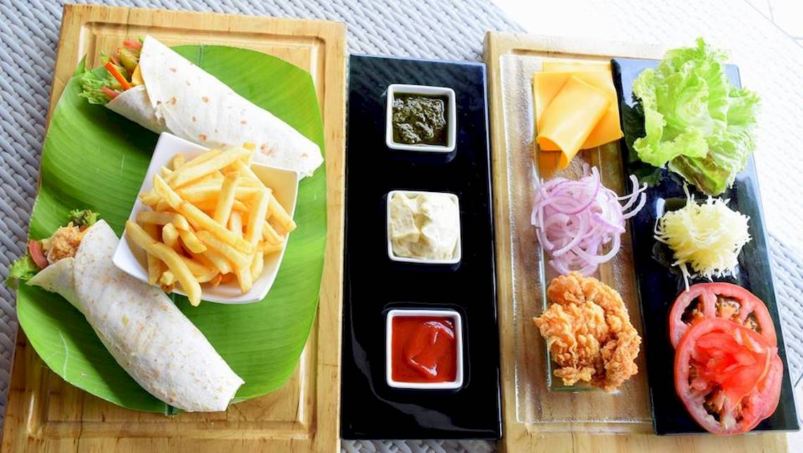 Essen Angebot des Hotels Tamassa Bel Ombre mit einem Burrito, Pommes, und Salat auf einem Blatt serviert.