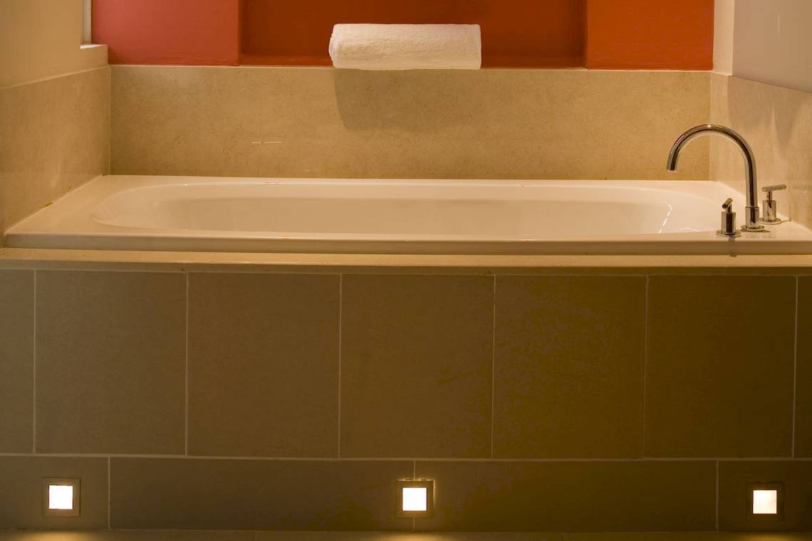 Badezimmer im Tamassa Bel Ombre Hotel mit Badewanne, Handtuchhalter und Beleuchtung.