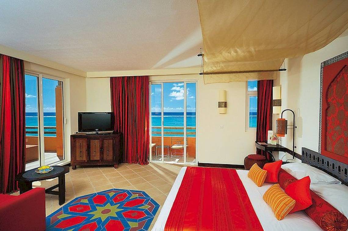 Hotelzimmer im SALT of Palmar mit Meerblick, rote Vorhänge und Bett, Fernseher und Tisch mit Balkon.