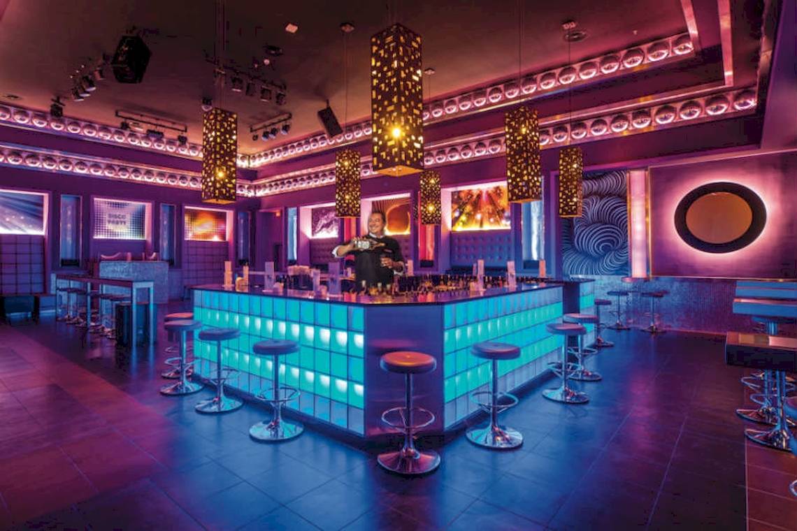 Innenansicht der Disco-Bar im Riu Cancun Hotel mit blauen Beleuchtungseffekten und einer Theke, an der ein Barkeeper steht.