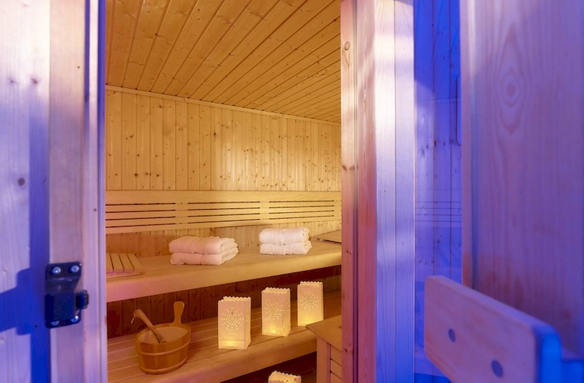 Innenansicht der Sauna im Astir Beach Hotel auf Kreta mit Holzbänken, weißen Handtüchern und dekorativen Laternen.