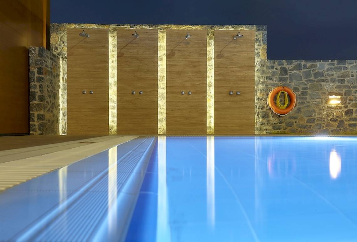 Ein leerer Pool im Astir Beach Hotel in Kreta mit Steinwänden und Duschen.