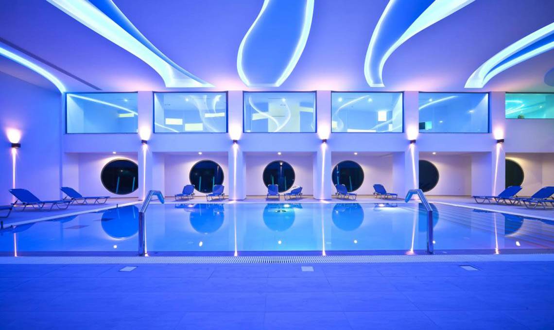 Ein modernes Schwimmbad im Kresten Royal Euphoria Resort mit blauen Leuchten und Lounge-Stühlen.