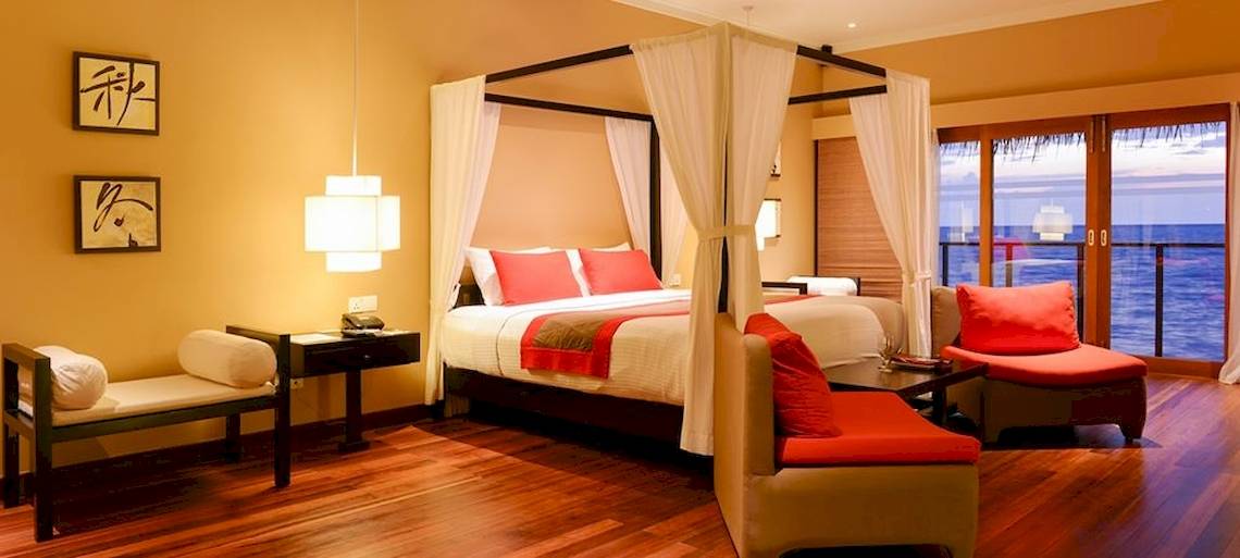 Hotelzimmer im Adaaran Select Hudhuran Fushi mit Himmelbett, Blick aufs Meer und modernem Interieur.