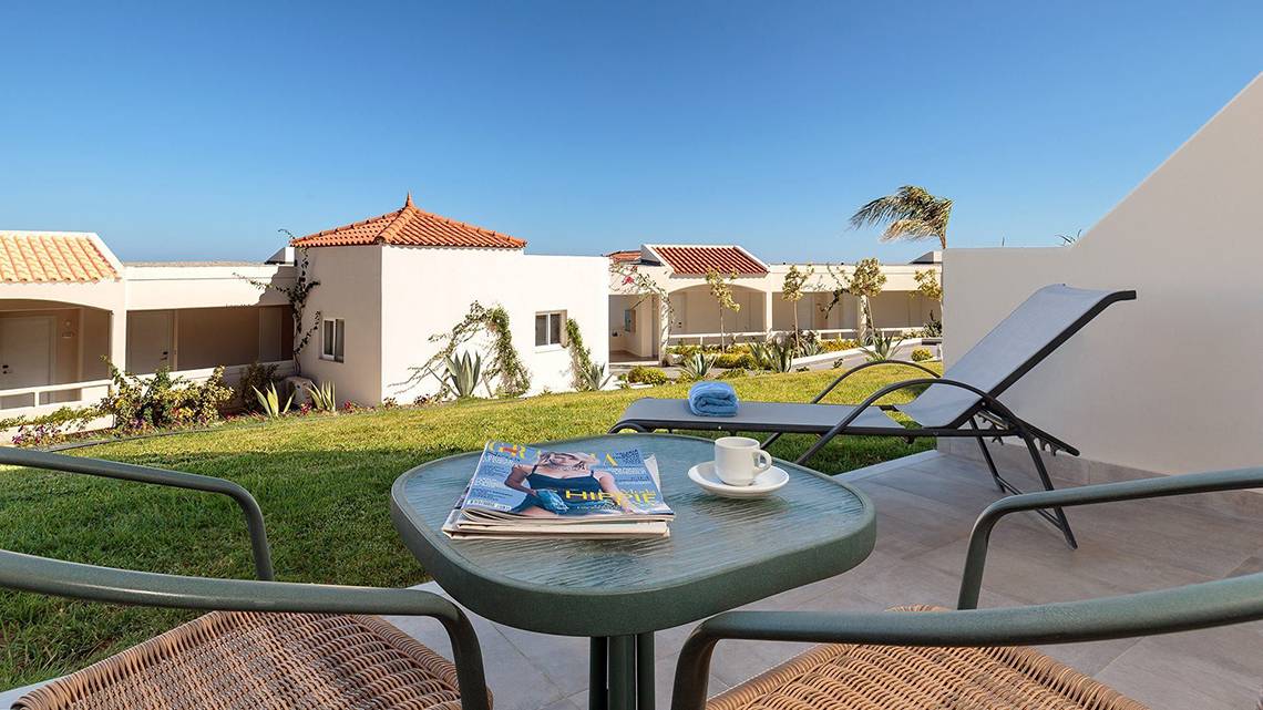 Außenbereich des Rodos Princess Beach Hotels mit Garten, Liegestühlen und Gebäuden im Hintergrund.
