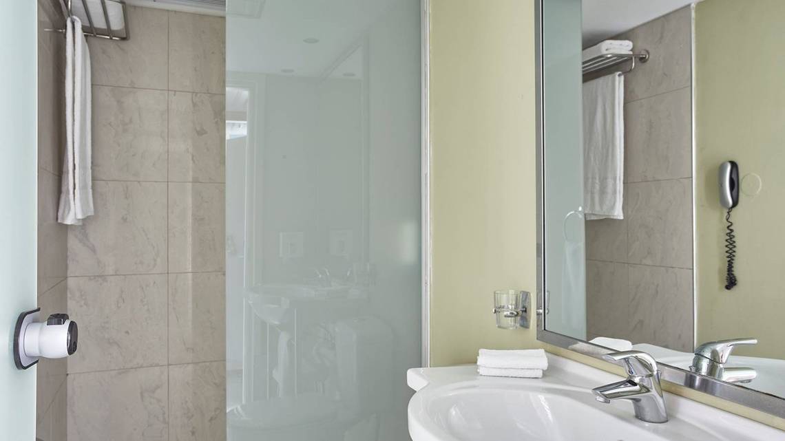 Badezimmer im Esperides Beach Resort mit Glasdusche, Waschbecken und Spiegel.